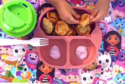 Baby Hands with Strawberry and Oatmeal Pancakes with Yogurt Served on a Silicone Pink Plate with a Green Cup and White Fork